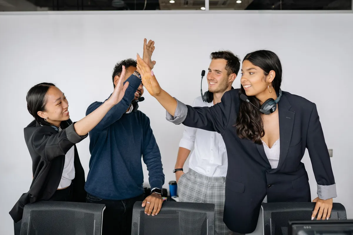 A sales team in headsets trading high fives at their desks